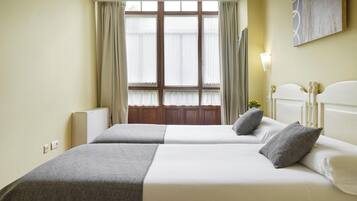 Habitación de hotel con dos camas, un ventanal con cortinas, un radiador y un cuadro en la pared.