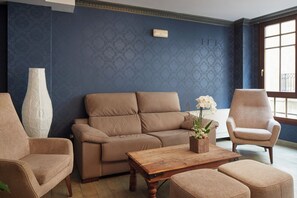 A living room with a sofa, two armchairs, a wooden coffee table, and a vase with flowers. - Iraipe Ongi Hotel (Oñati)