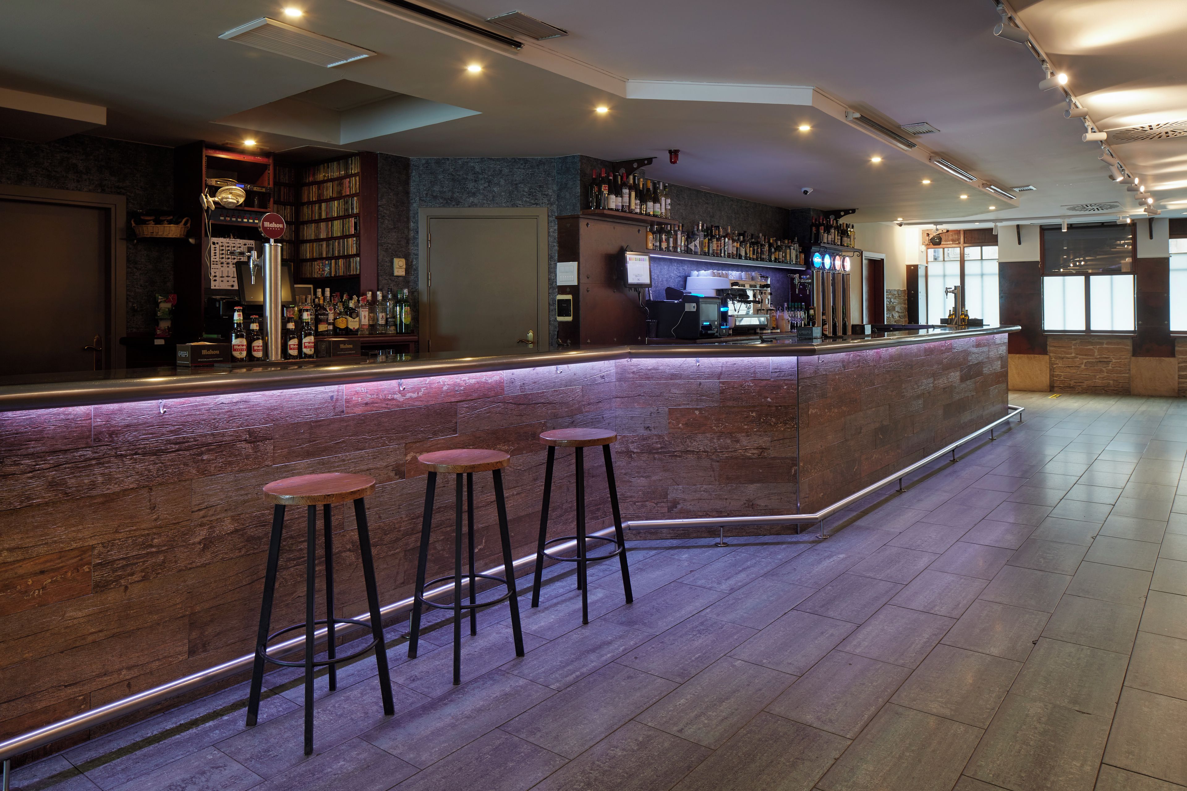 A bar area with a counter, stools, and a variety of bottles.