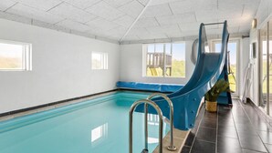 Ein Hallenbad mit einer blauen Rutsche, einer Sitzbank und Blick ins Freie durch große Fenster.