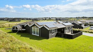 Eine Reihe moderner, eingeschossiger Blockhütten mit Solaranlagen auf den Dächern, gelegen in einer grünen Wiese unter blauem Himmel.
