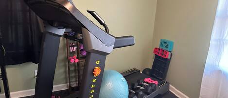 Un gimnasio en casa con cinta de correr, pelota de ejercicios y mancuernas.