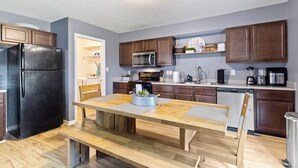 A modern kitchen with wooden cabinets, a black refrigerator, a dining table with benches, and a microwave. - Splendid 4 Bed/2.5 Bath- Near Speedway (Indianapolis)