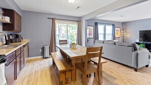 A modern kitchen with wooden countertops, a dining table, and a bench. There is a grey sofa in the living area with a flat-screen TV. - Splendid 4 Bed/2.5 Bath- Near Speedway (Indianapolis)