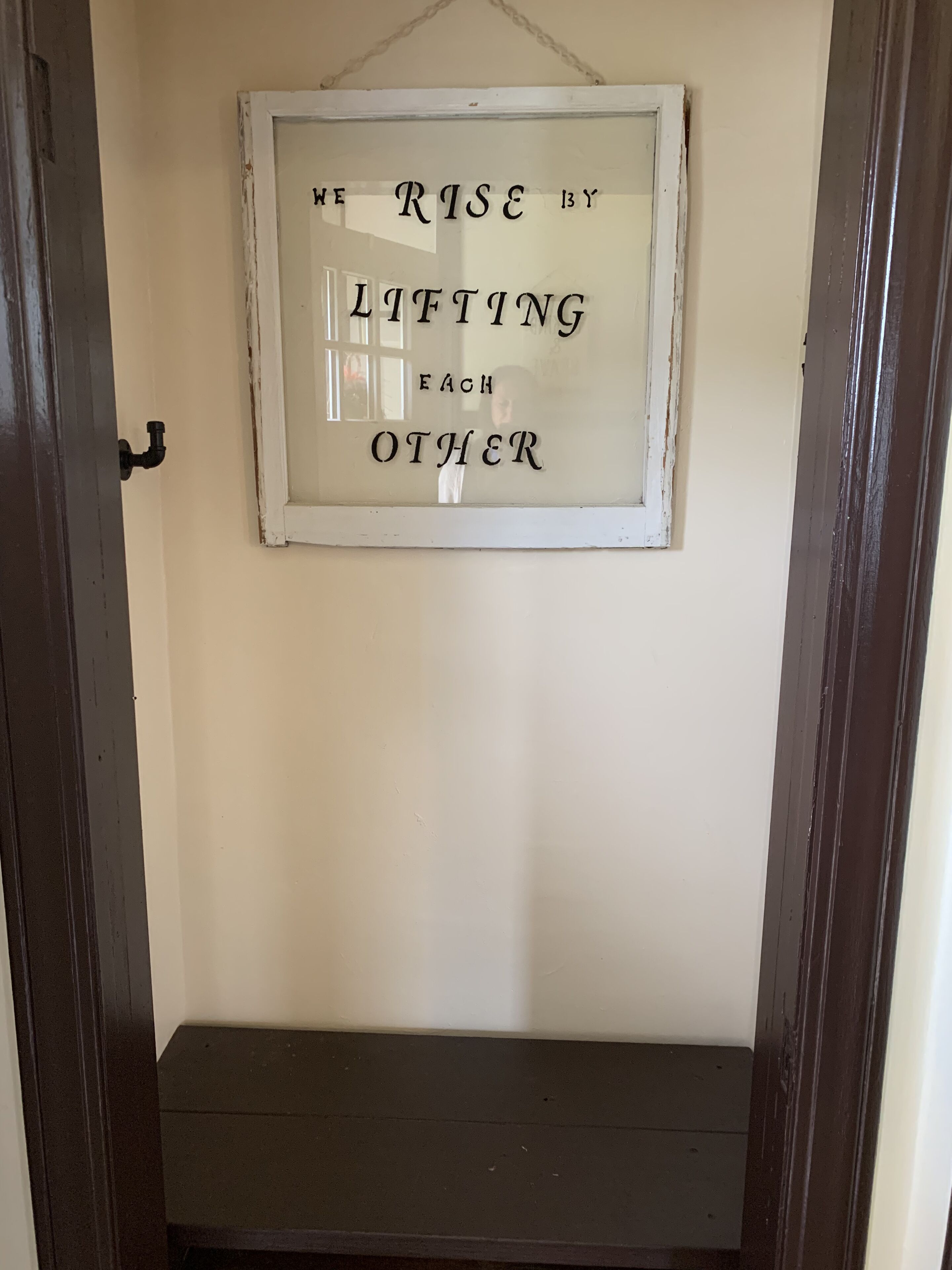 A framed quote on a wall in a room with a dark door and a small shelf below.