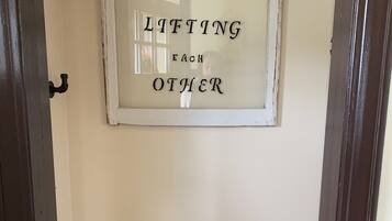 A framed quote on a wall in a room with a dark door and a small shelf below.