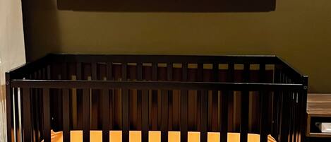 A crib with an orange mattress, a striped blanket, and two framed abstract paintings on the wall above.