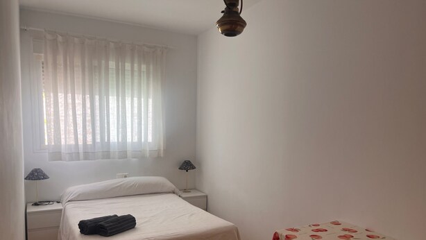 Une chambre à coucher avec un lit, des lampes de chevet, une table ornée d’un motif de fruits et une fenêtre avec des rideaux légers.