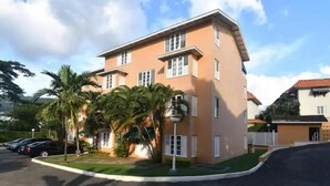 A two-story building with a flat roof and white window shutters, surrounded by palm trees and a clear sky. - Captivating 1-Bed  Ravinia Apartment in Kingston (Kingston)