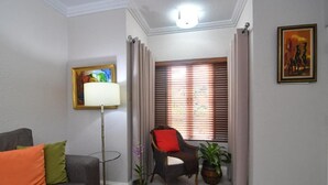 A living room with a grey sofa, a floor lamp, a chair with a red cushion, and a window with blinds. - Captivating 1-Bed  Ravinia Apartment in Kingston (Kingston)