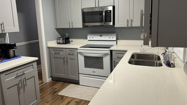 A modern kitchen with grey cabinets, a stainless steel microwave, a toaster, a stove, and a sink. - Mountain View Home (Cave Spring)
