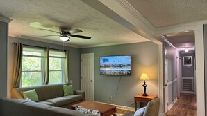 A living room with a sofa, a coffee table, a TV mounted on the wall, and a ceiling fan. - Mountain View Home (Cave Spring)