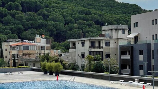 A rooftop pool with a view of a forested hill, modern buildings, and a clear sky. - Tilal Fanar resort, pools, generator included (Fanar)