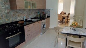 A modern kitchen with a gas stove, microwave, and washing machine. There is a dining area with a table and chairs. - Tilal Fanar resort, pools, generator included (Fanar)