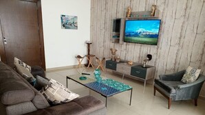 A living room with a sofa, armchair, coffee table, TV, and decorative items. - Tilal Fanar resort, pools, generator included (Fanar)