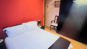 A bed with white linens, a nightstand with a lamp, and a chair in a room with red walls and a dark wardrobe. - 2 Bed-Sleeps5-Free Parking-10 min Walk underground (London)