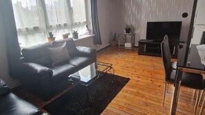 A living room with a black leather sofa, a TV, and a small table with potted plants. - 2 Bed-Sleeps5-Free Parking-10 min Walk underground (London)