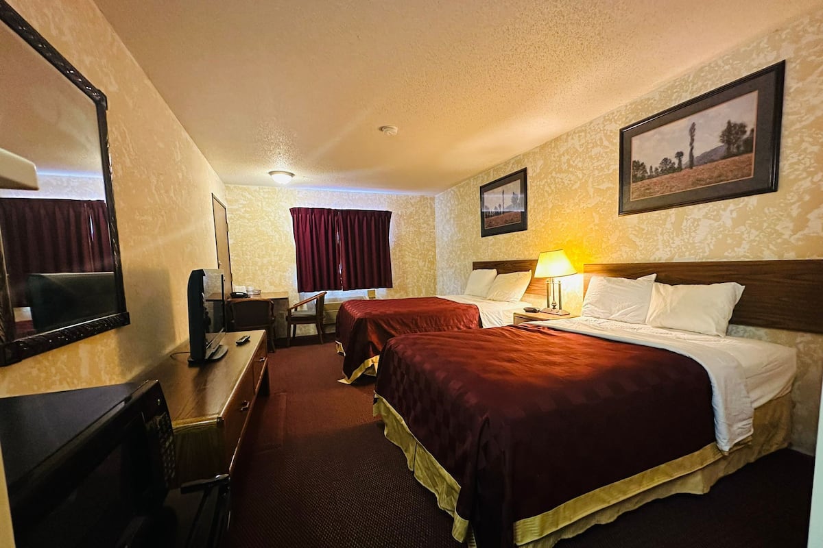 A hotel room with two beds, a desk, a chair, a television, and a window with curtains.