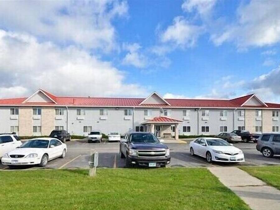 A multi-story hotel with a red roof, several parking spaces, and a grassy area in front.