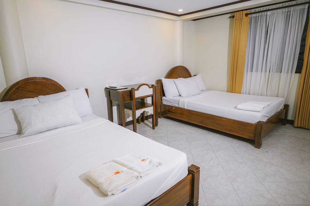 A hotel room with two single beds, a wooden desk, and a chair.