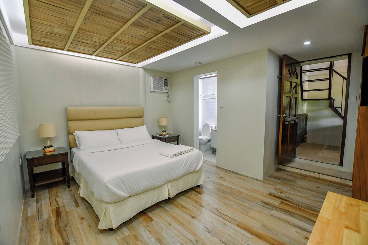 A bedroom with a large bed, bedside tables, a ceiling fan, and a wooden floor.