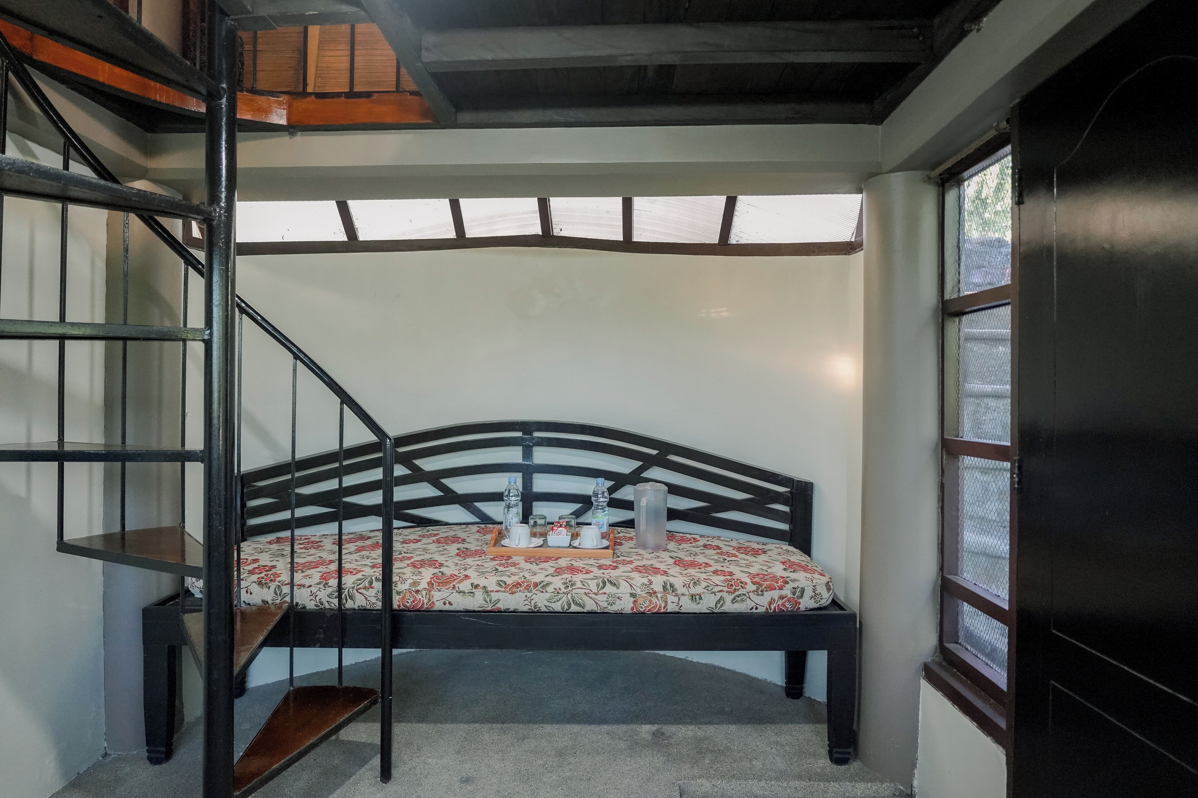 A bedroom with a bed, a small table with a tray, a window, and a staircase.