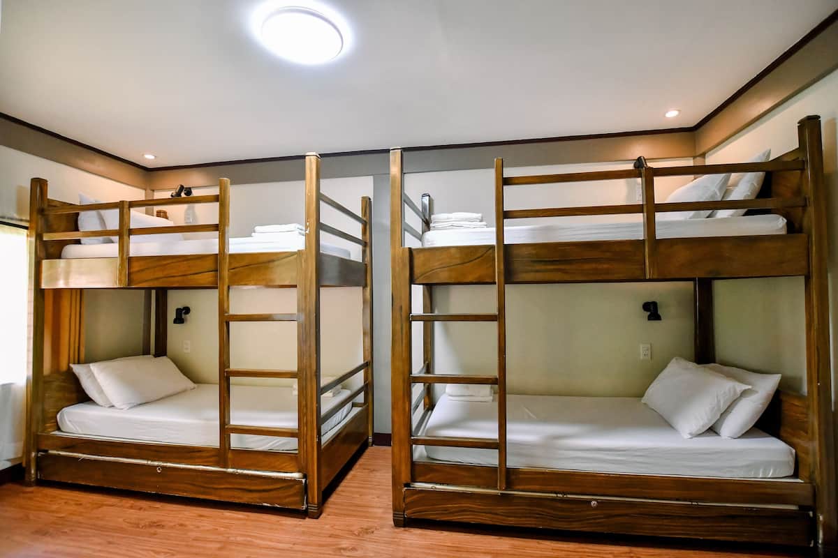 A room with two bunk beds, wooden frames, white bedding, and a ceiling light.