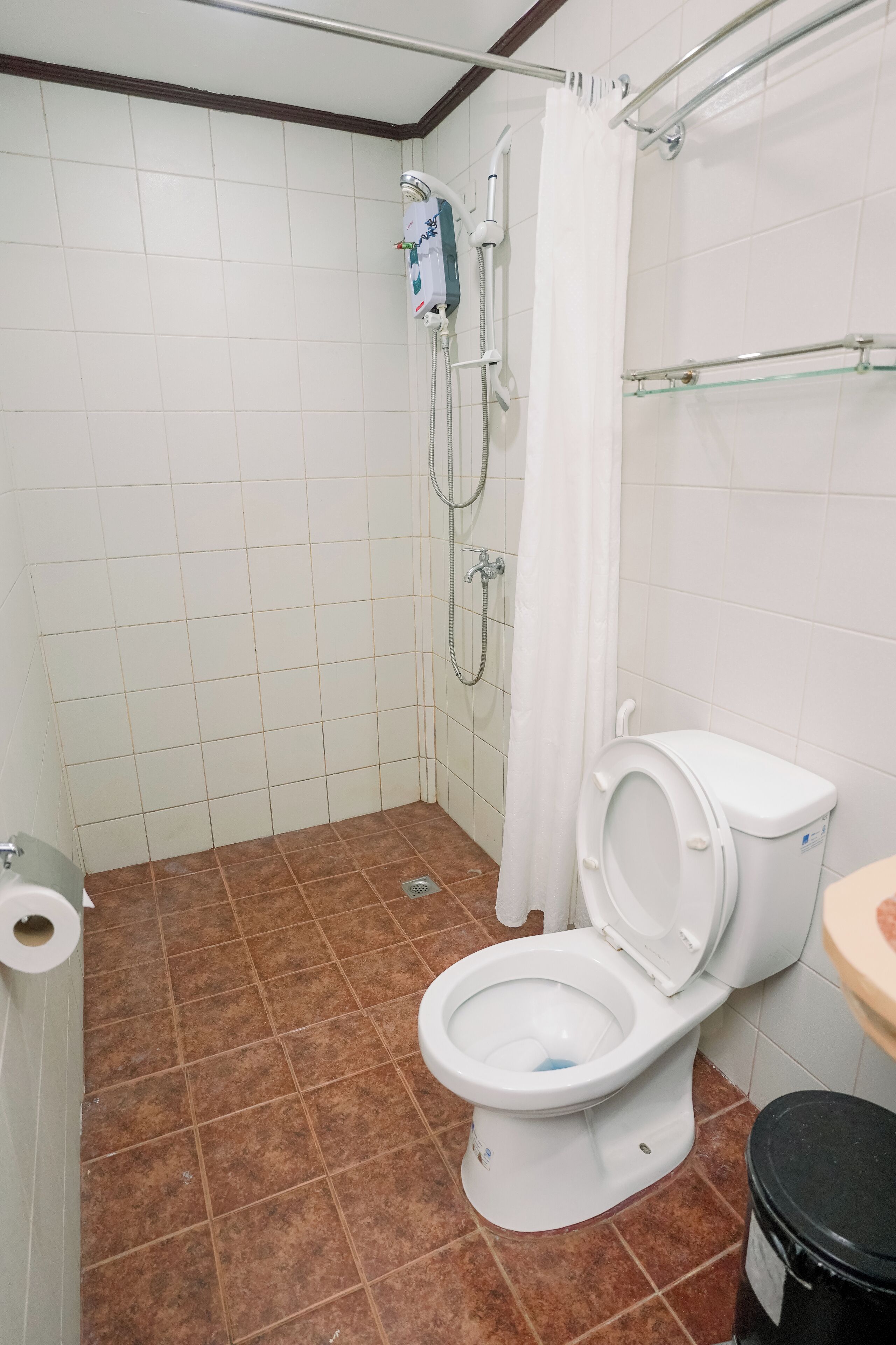Un baño con inodoro blanco, ducha con repisa de vidrio y suelo de baldosas marrones.