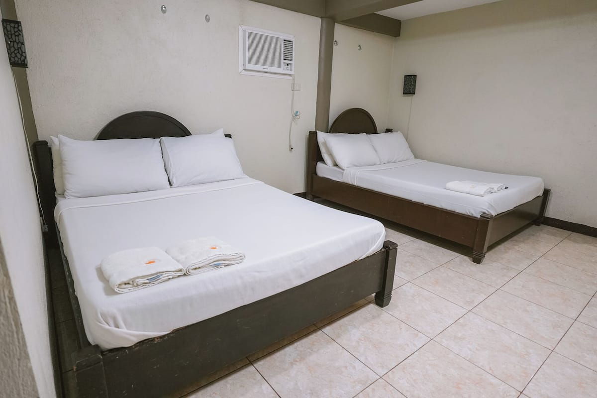 Two single beds with white linens and towels, a wall-mounted air conditioner, and a tiled floor.
