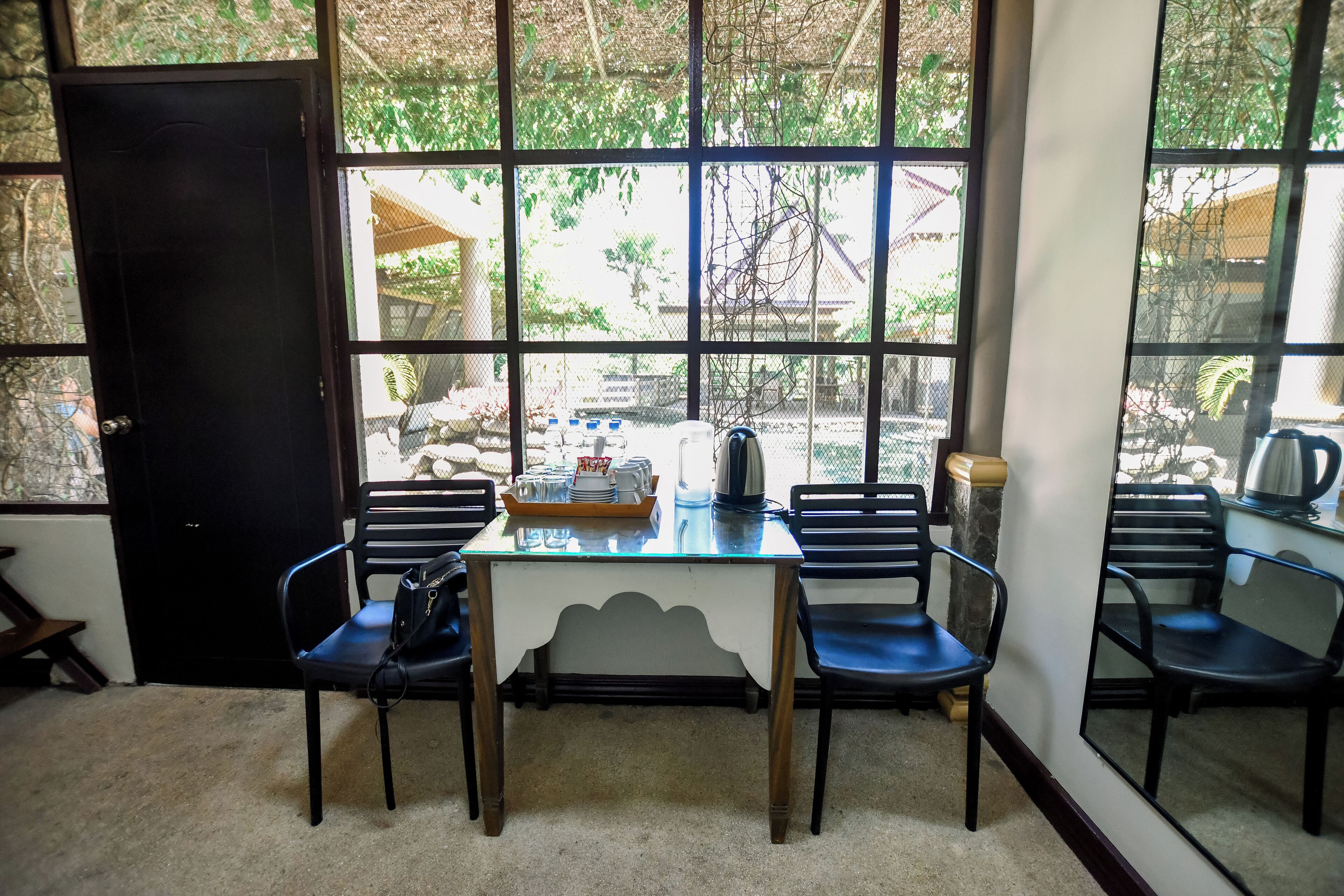 A room with a table and four chairs, a door, and large windows with a view of the outside.