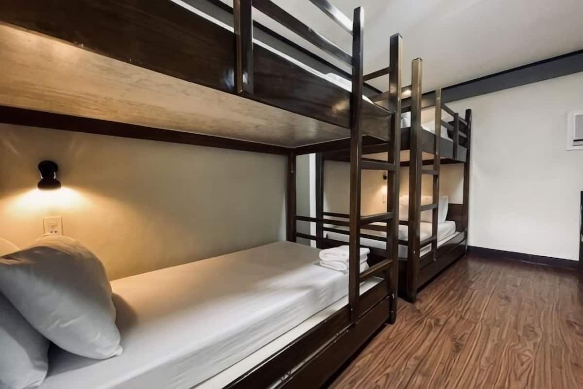 A bunk bed room with a wooden floor, a wall-mounted light, and a power outlet.