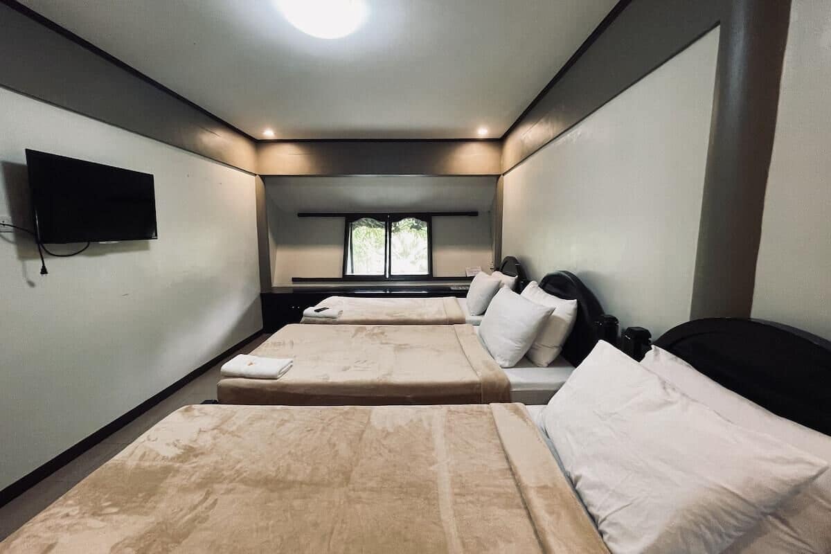 A hotel room with two beds, a TV, a window, and a desk.