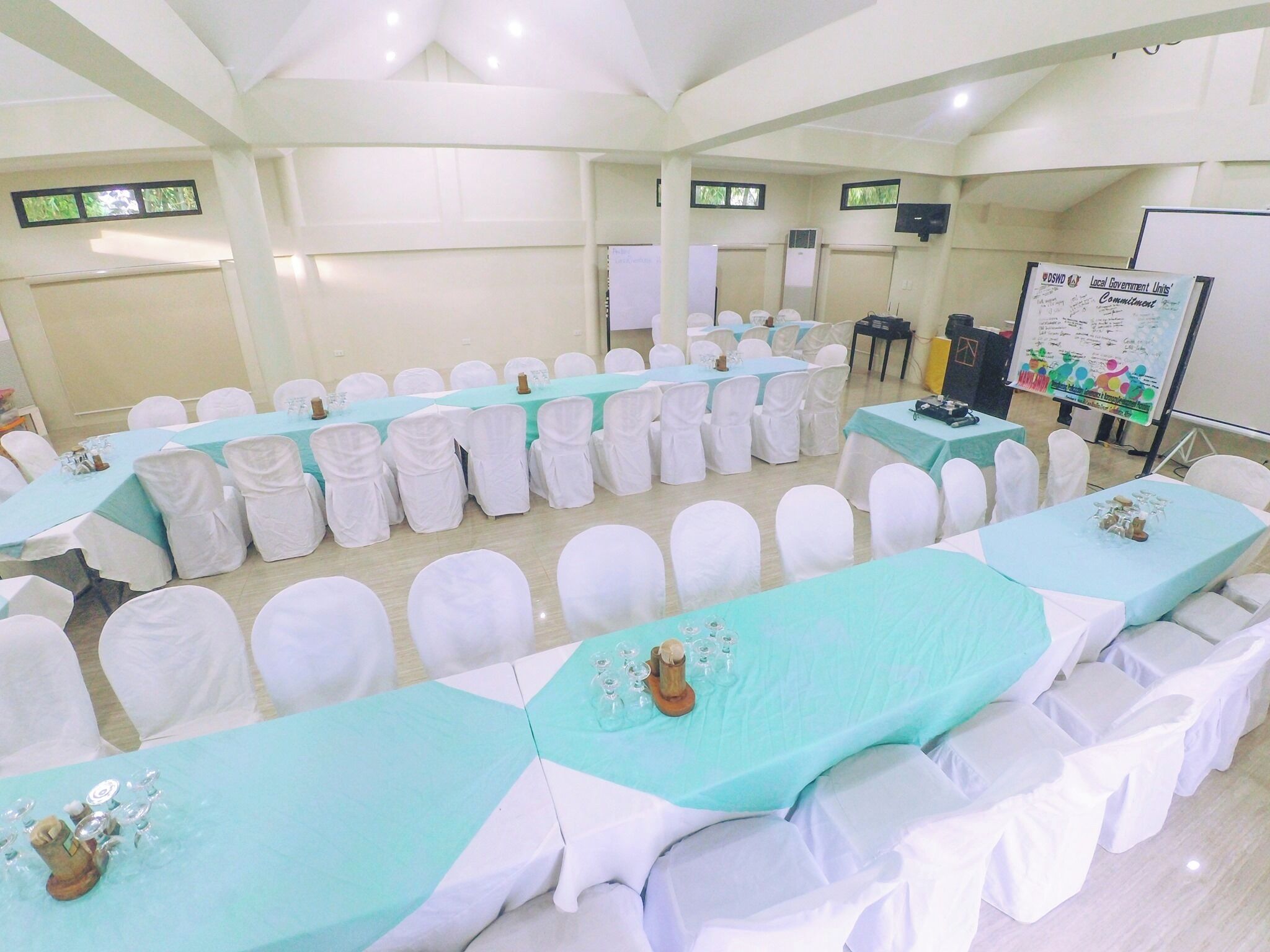 Un salón de conferencias con filas de sillas blancas y mesas cubiertas con manteles azul claro.