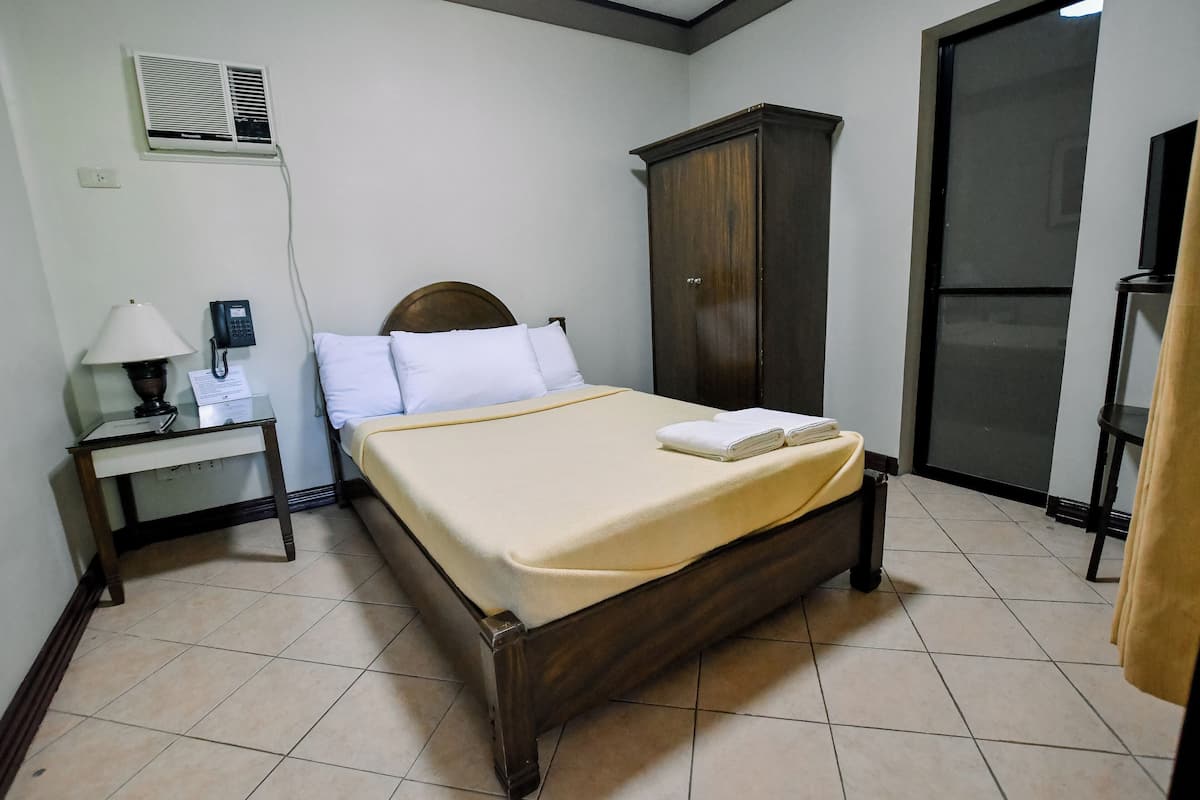 A hotel room with a bed, a desk with a lamp, a phone, a wardrobe, and a sliding door.