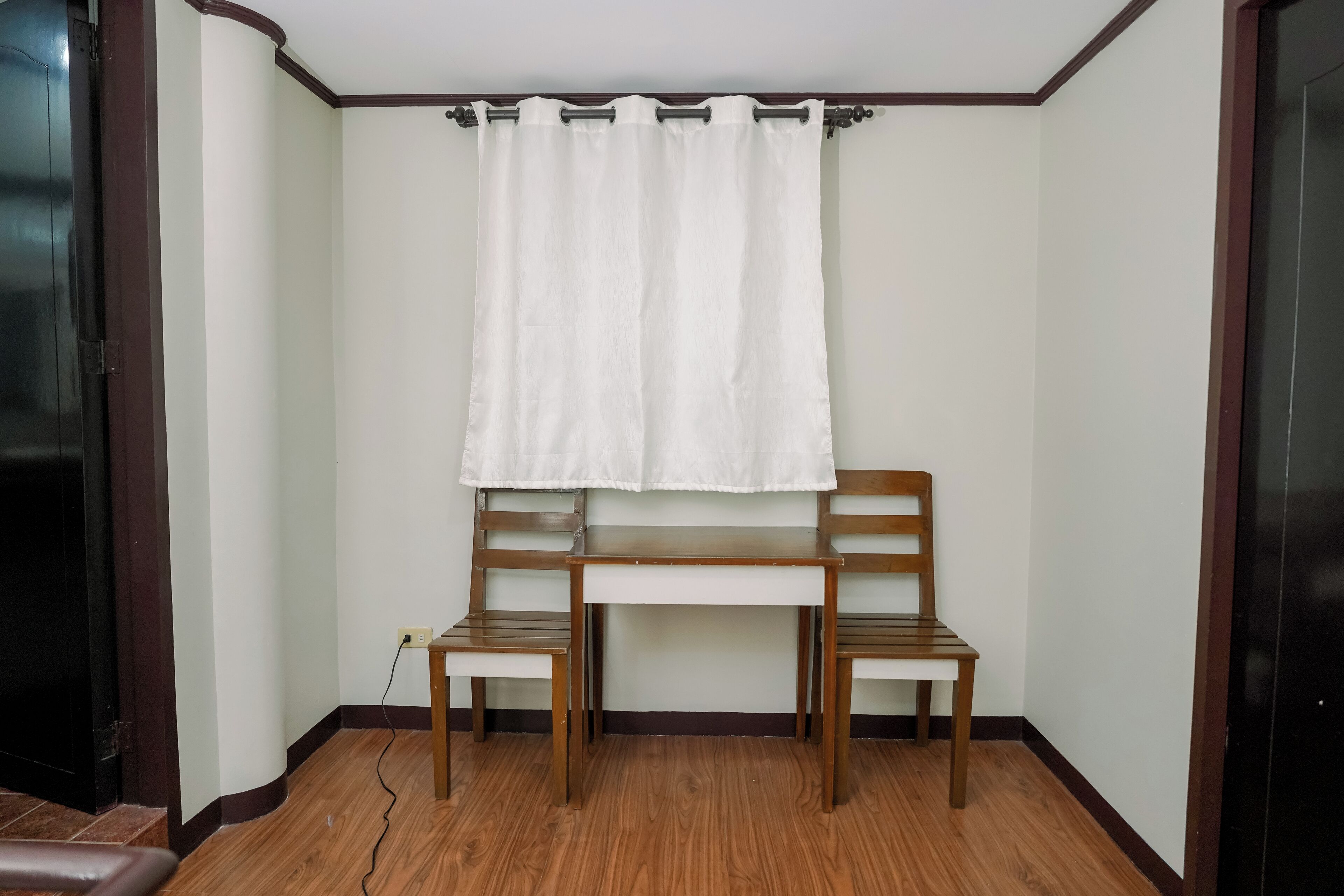 Una habitación con un banco de madera, una cortina blanca y un enchufe.
