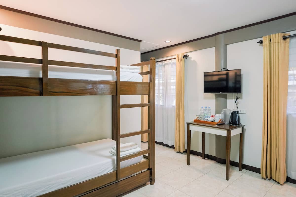 A bunk bed room with a TV, a table with a kettle, and curtains.