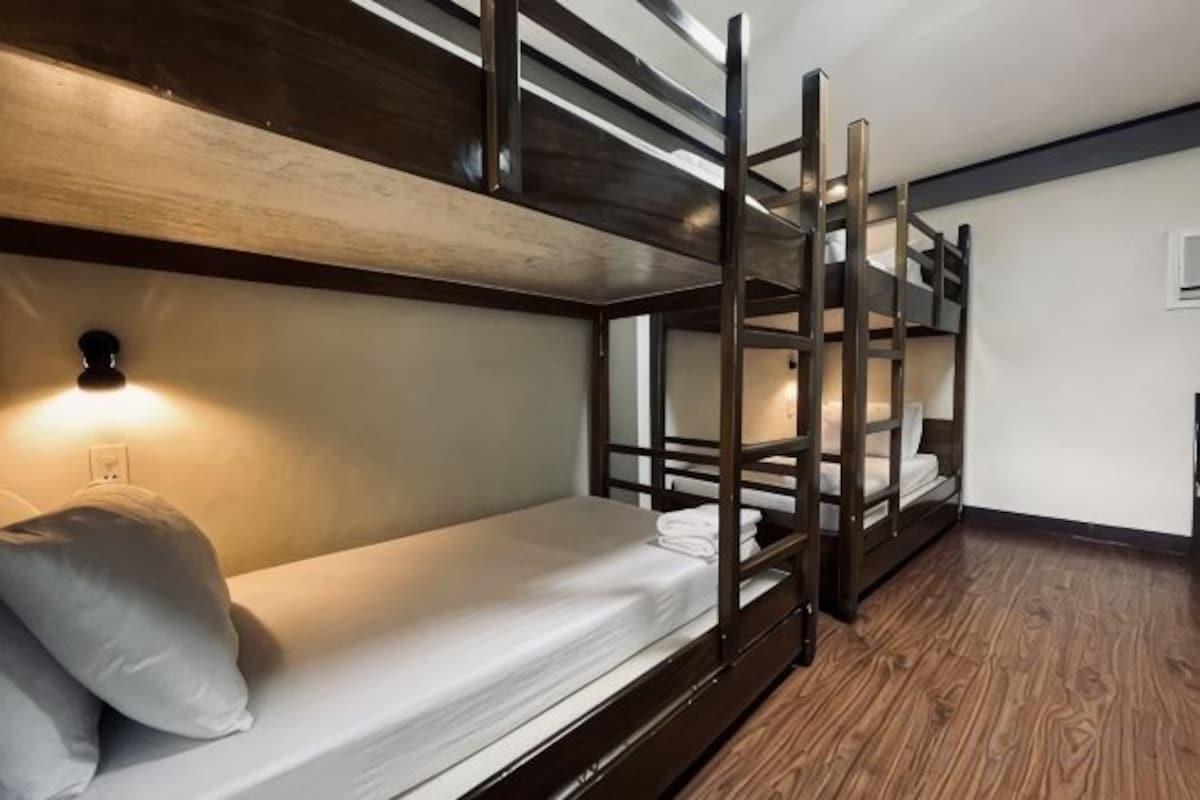 A bunk bed room with a wooden floor, a wall-mounted light, and a power outlet.