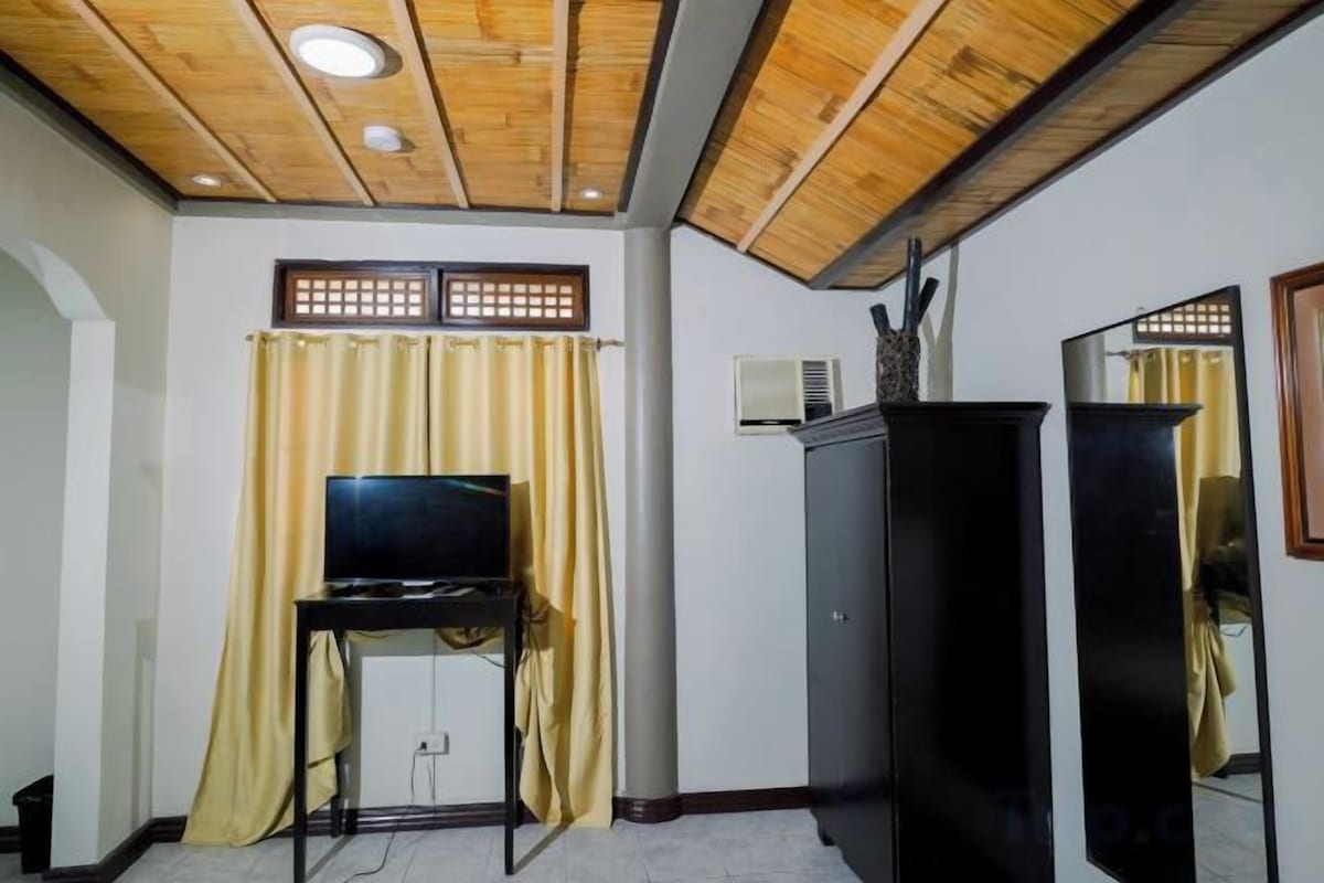 A room with a wooden ceiling, a television on a stand, a cabinet, and a mirror.