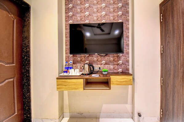 A modern bathroom with a flat-screen TV mounted above a wooden vanity, a small sink, and a decorative backsplash.