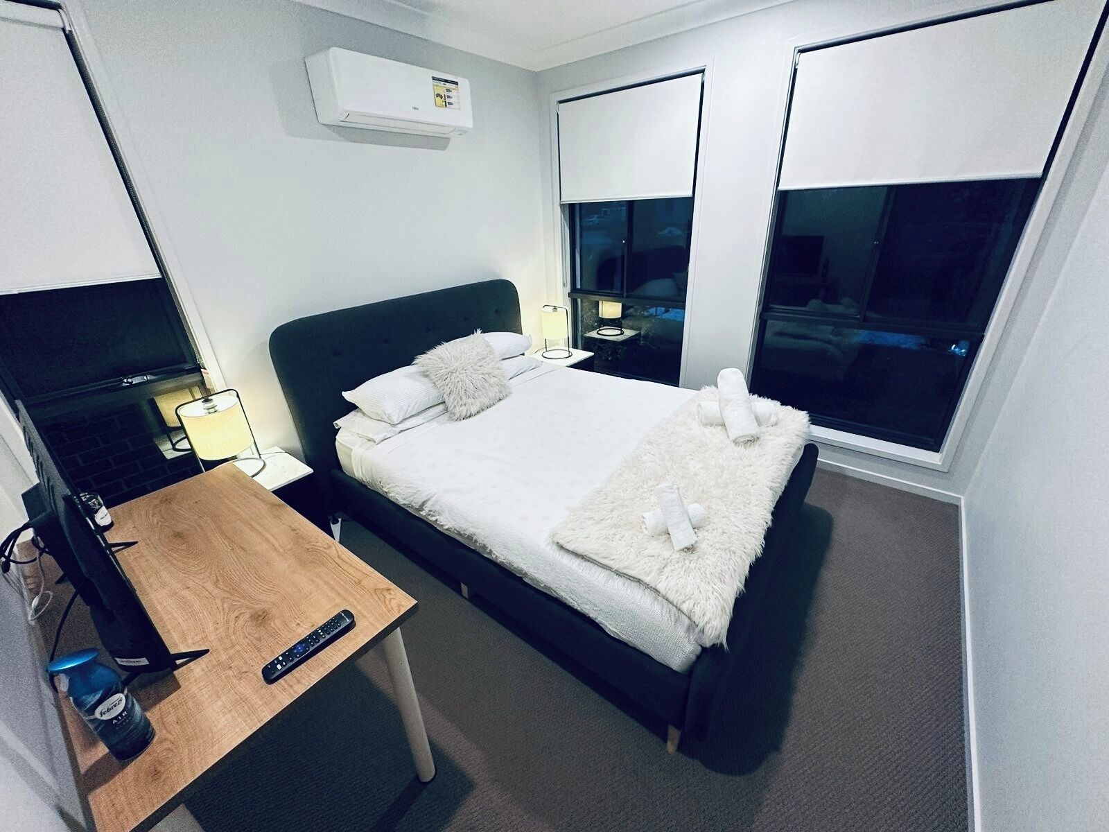 A modern hotel room with a single bed, a desk with a laptop, a TV, and a large window.