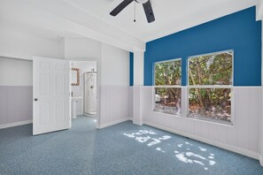Un pasillo con ventilador de techo, una puerta que da a un baño y una ventana con vistas a árboles.