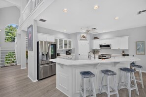 A modern kitchen with white cabinetry, stainless steel appliances, and a large island with bar stools.