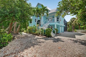 A two-story house with a staircase leading to the upper floor, surrounded by lush greenery and a gravel driveway.