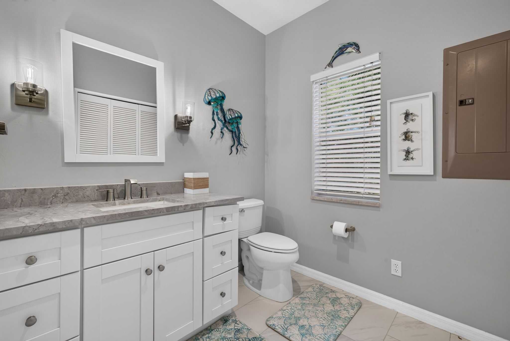 A bathroom with a white vanity, a toilet, a shower, and a wall-mounted light fixture.