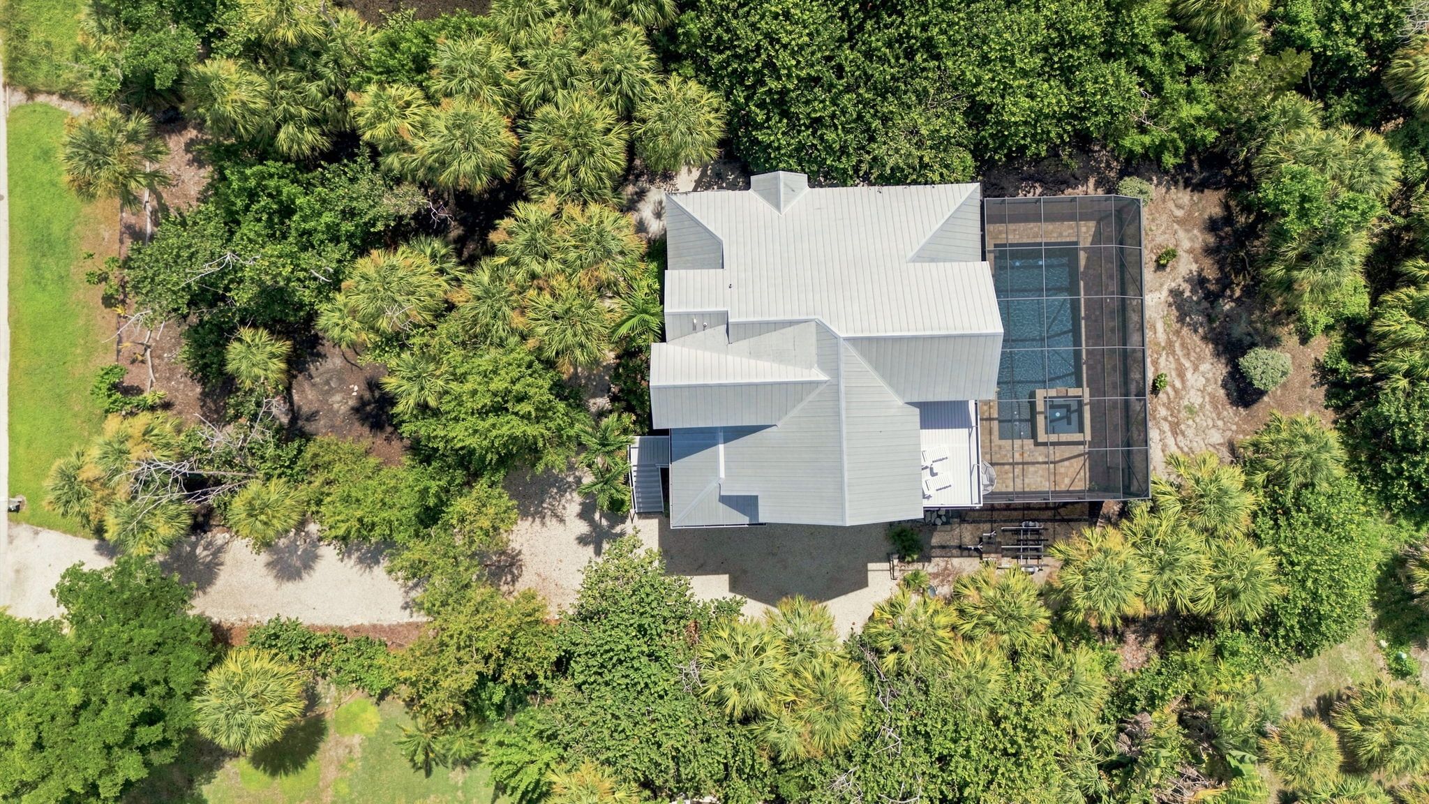 An aerial view of a modern house with a large deck, surrounded by dense greenery.
