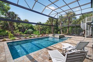 A swimming pool with a glass enclosure, surrounded by lounge chairs and a small hot tub.