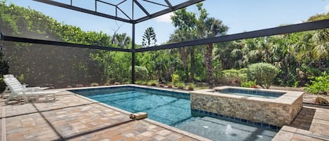 Une piscine extérieure dotée d’une structure en verre, entourée d’un patio avec un sol en briques et des chaises longues.