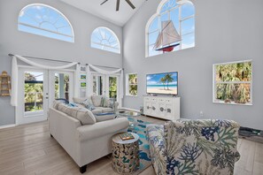 A spacious living room with a large sofa, a patterned armchair, a TV, and a sailboat decoration. - Huge savings for March April and May! (Sanibel)