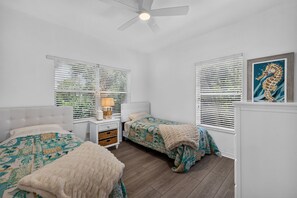 Un dormitorio con dos camas, ventilador de techo y ventana con persianas.
