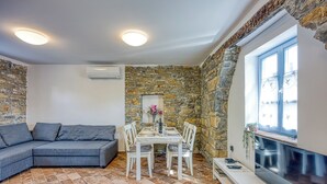 Un salon chaleureux avec un mur en pierre, un canapé gris, une table à manger avec des chaises et un téléviseur à écran plat fixé au mur.